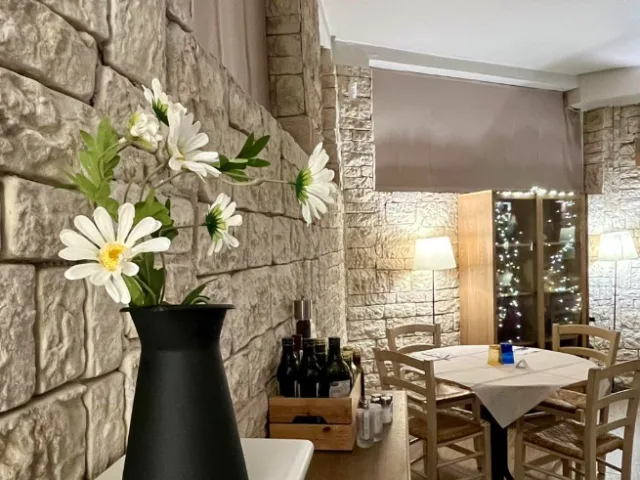 Sala del Theorema Ristorante Pizzeria a Pero, con pareti in pietra a vista, margherite bianche e tavoli apparecchiati in un ambiente accogliente.