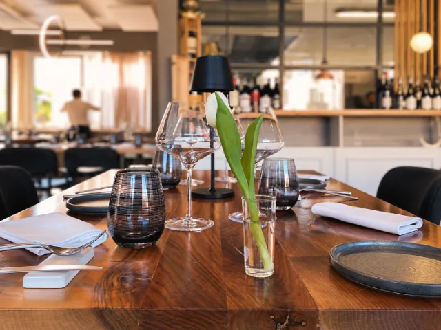 Tavolo apparecchiato nella sala del Ristorante Ossobuco a Varese, con calici, piatti, tovaglioli e decorazione floreale.