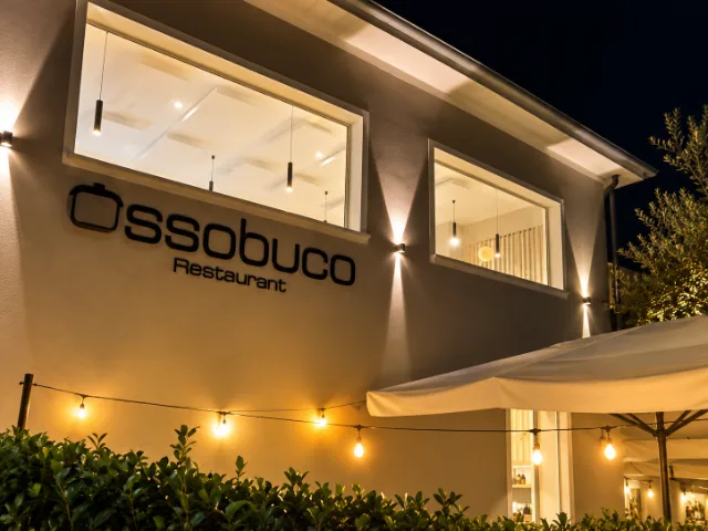 Facciata esterna del Ristorante Ossobuco a Varese, illuminata di sera, con insegna e finestre del locale.