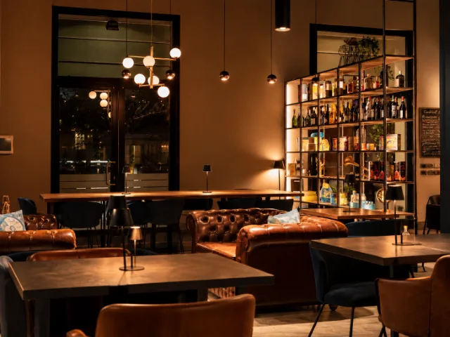 Interni di SIMUL Restaurant & Drink a Crema, con divani in pelle, tavoli, lampade a luce soffusa e scaffalature con bottiglie, in un ambiente elegante e accogliente.