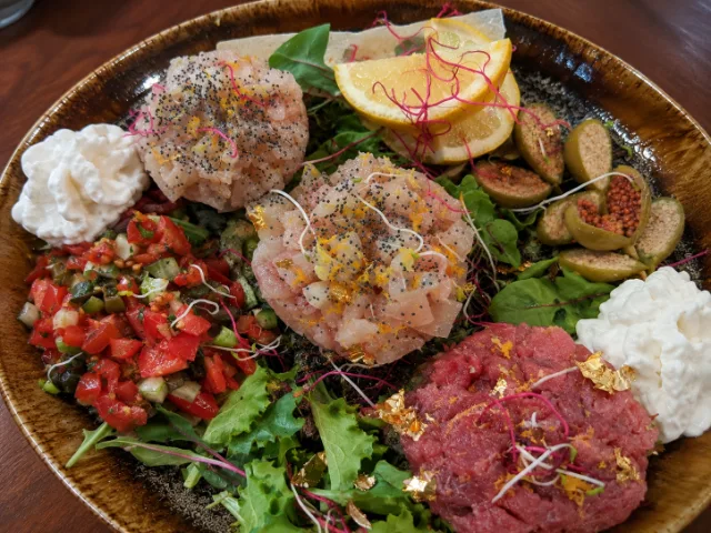 Selezione di tartare di pesce del Dai Tosi Bistrò, accompagnate da verdure fresche, fichi, agrumi e guarnizioni, servite su un piatto in ceramica.