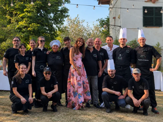 Foto di gruppo dello staff della Trattoria Il Paladino di Alessandria insieme a un'ospite speciale, durante un evento all'aperto, con cuochi e personale di sala riuniti in un'atmosfera conviviale.