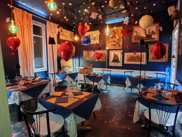 Sala interna della Trattoria Il Paladino ad Alessandria, con tavoli apparecchiati, pareti blu decorate con quadri, stelle e pianeti sospesi, cuori rossi e luci colorate che creano un'atmosfera originale e accogliente.