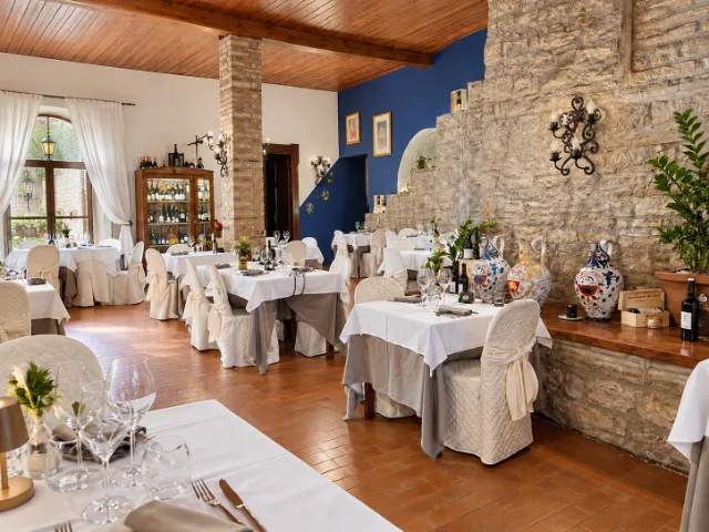 Sala interna del Ristorante Conte Fabiani a Gubbio, con pareti in pietra, soffitto in legno, tavoli elegantemente apparecchiati e illuminazione naturale del giorno che valorizza l'atmosfera storica del locale.