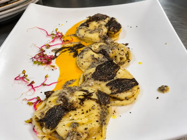 Pasta ripiena al tartufo del Ristorante Conte Fabiani a Gubbio, servita con salsa cremosa, scaglie di tartufo nero e germogli su un piatto bianco, con una presentazione curata nei dettagli.