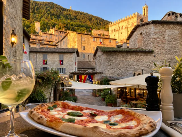Pizza Margherita servita sulla terrazza del Ristorante Conte Fabiani a Gubbio, con vista sui palazzi medievali del centro storico illuminati dalla luce del tramonto.