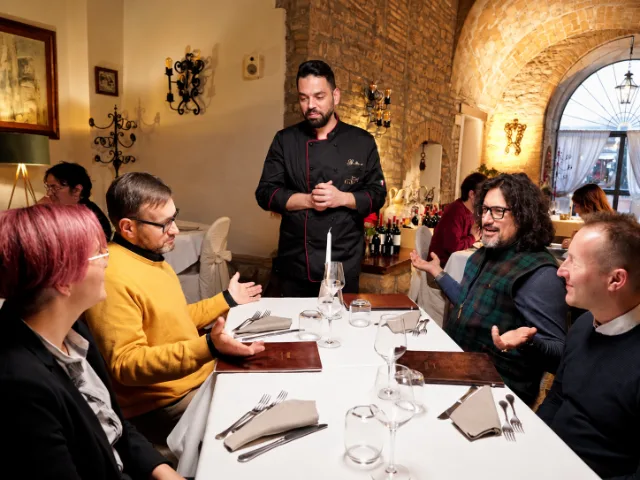 Lo Chef Gaetano del Ristorante Conte Fabiani a Gubbio durante la partecipazione ad Alessandro Borghese 4 Ristoranti, insieme agli altri ristoratori riuniti a tavola nella sala storica del locale.