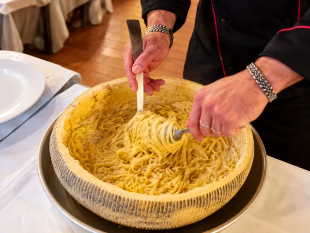 Lo Chef Gaetano del Ristorante Conte Fabiani a Gubbio mentre manteca gli spaghetti all'interno di una forma di formaggio, mostrando la preparazione del piatto direttamente al tavolo.