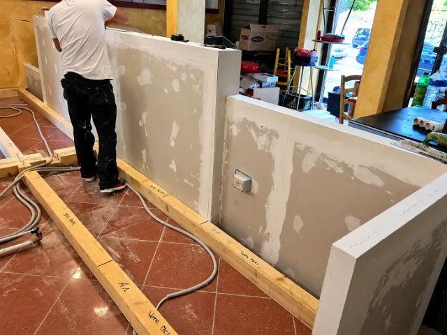 Lucrător care construiește un tejghea pentru un spațiu comercial, cu structura în curs de amenajare și materiale de construcție.