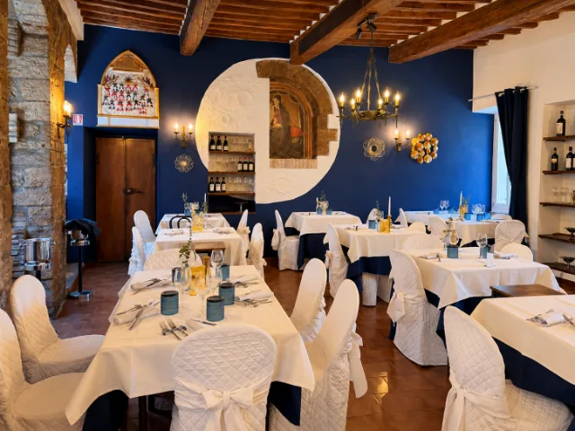 Sala interna del Ristorante Duca Federico da Montefeltro a Gubbio, con travi in legno a vista, pareti blu, dettagli storici e tavoli elegantemente apparecchiati.