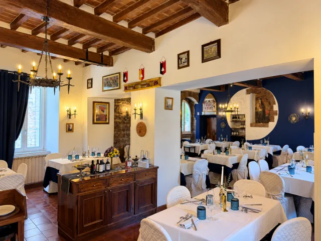 Sala interna del Ristorante Duca Federico da Montefeltro a Gubbio, con travi in legno a vista, tavoli elegantemente apparecchiati e pareti blu con dettagli storici.