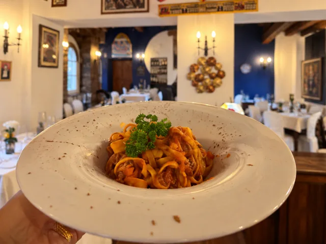 Tagliatelle al sugo d’oca servite in un piatto di ceramica, con prezzemolo fresco, nella sala del Ristorante Duca Federico da Montefeltro a Gubbio.
