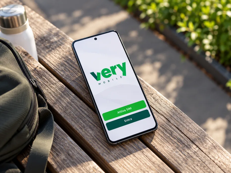Smartphone με το λογότυπο Very Mobile και επιλογές ενεργοποίησης SIM στην οθόνη, ακουμπισμένο σε ξύλινο παγκάκι σε εξωτερικό χώρο.