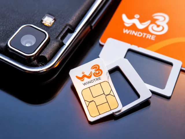 Scheda SIM WINDTRE con logo arancione e contatti dorati, affiancata da adattatori SIM e uno smartphone su una superficie scura.
