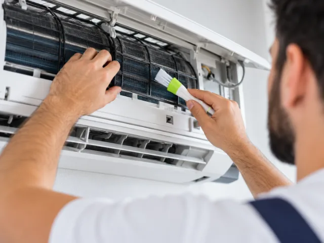 Tecnico durante la pulizia del filtro interno di un condizionatore a parete mediante una spazzola per la manutenzione.