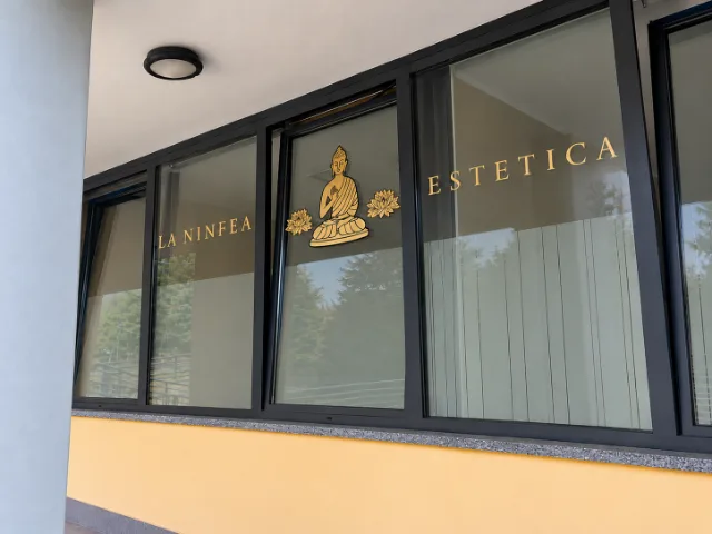 Vetrina esterna del Centro Estetico La Ninfea a Induno Olona, con insegna dorata e decorazioni raffiguranti Buddha e fiori di loto.