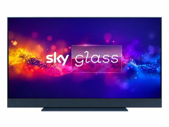 Televisore Sky Glass in primo piano su sfondo bianco, con design sottile, base elegante e logo Sky Glass al centro dello schermo, accompagnato da effetti luminosi nelle tonalità arancione, rosa, viola e blu.