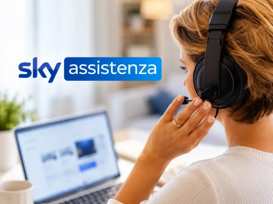 Operatrice con cuffie e microfono davanti a un computer, in un ambiente moderno e luminoso, con logo Sky Assistenza in primo piano.